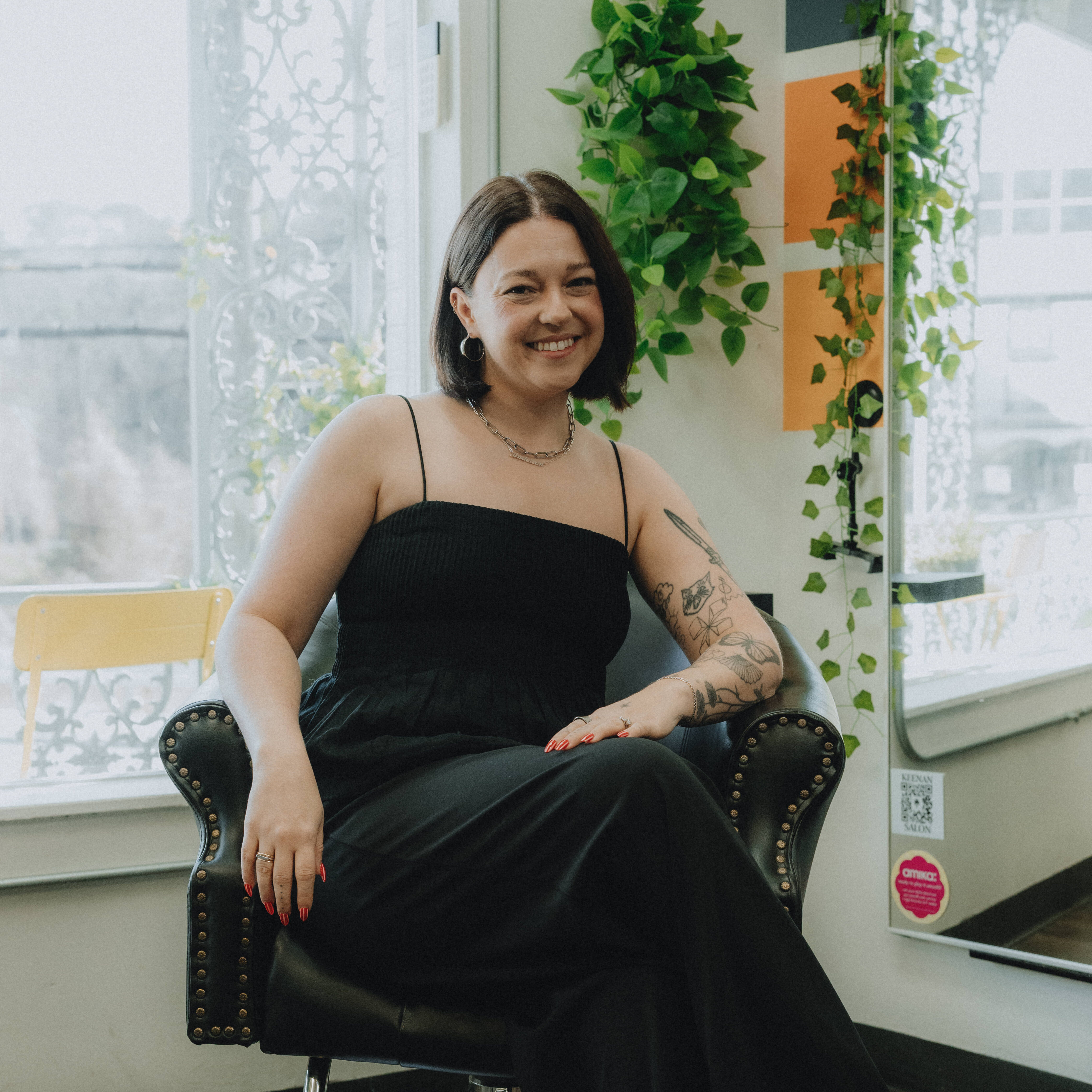 Keenan Salon 2026 Quinn, stylist at Keenan Salon, sitting comfortably in a salon chair wearing a red sweater, specializing in stylish bobs, keratin smoothing treatments, and low-maintenance cuts in Atlanta.