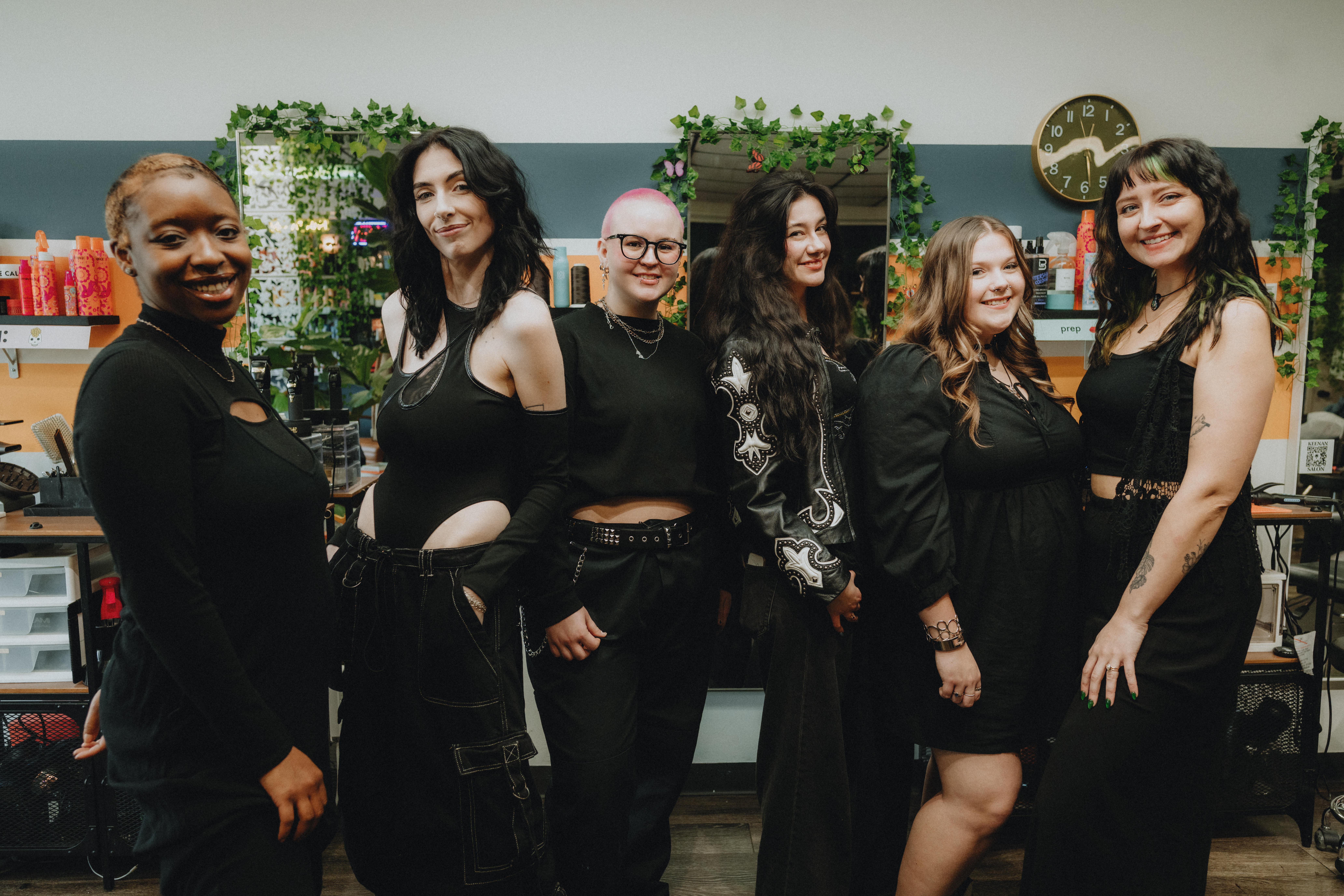 Keenan Salon 2026 The Keenan Salon team posing together in the salon, featuring stylists dressed in black with a backdrop of colorful hair products and plants.