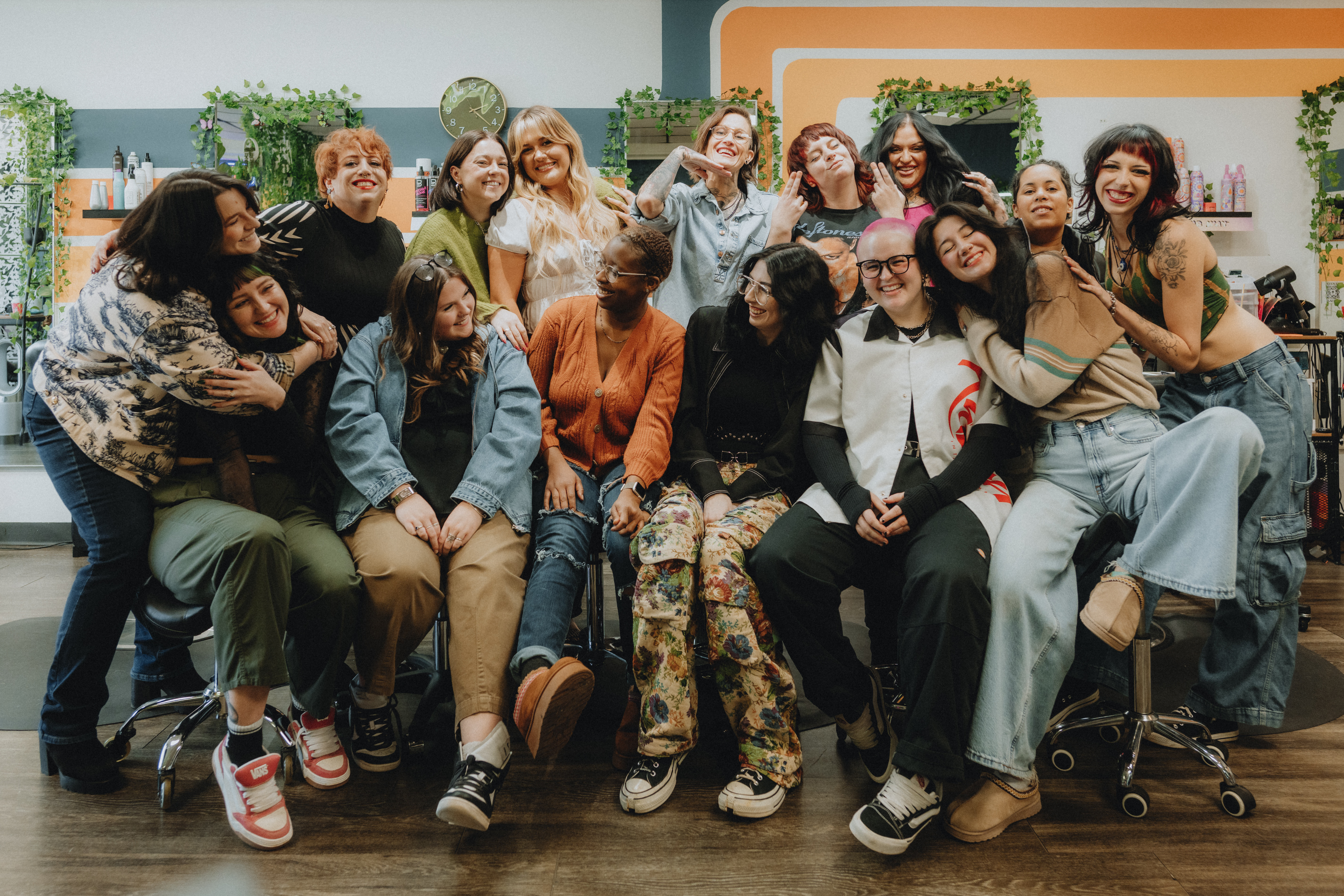 The Keenan Salon team posing together in the salon, featuring stylists dressed in black with a backdrop of colorful hair products and plants.