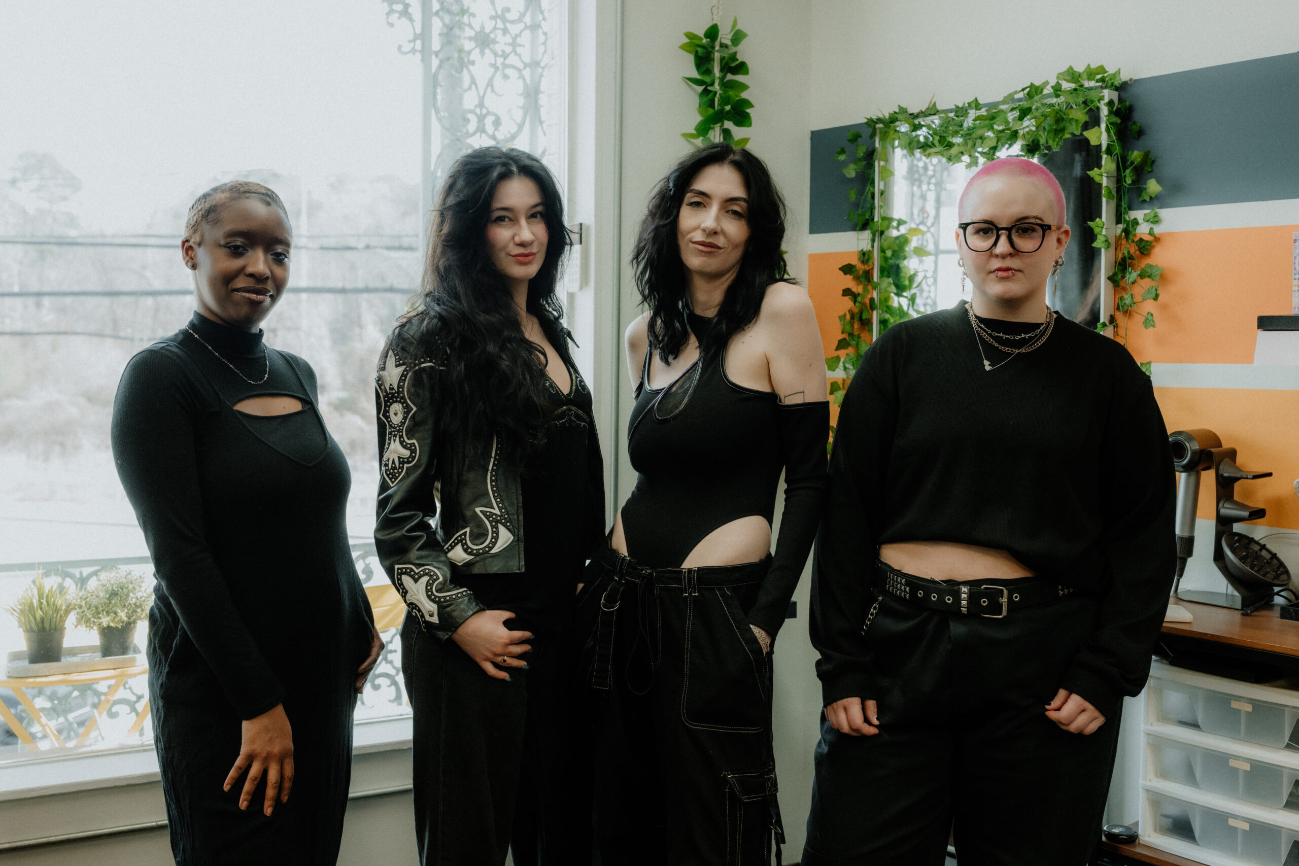 The Keenan Salon team posing together in the salon, featuring stylists dressed in black with a backdrop of colorful hair products and plants.